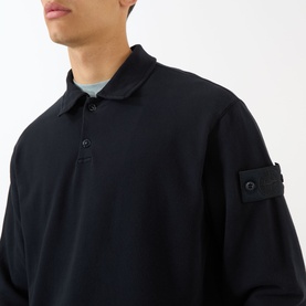 Model wearing navy long-sleeve polo shirt with collar, button placket, and branded sleeve badge detail, styled with a light blue underlayer.