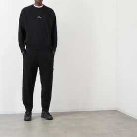 Model wearing Stone Island black polyester sweatshirt with chest logo, styled with matching black joggers and chunky trainers.
