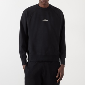 Model wearing Stone Island black crew neck sweatshirt with small chest logo, styled with matching black shorts.