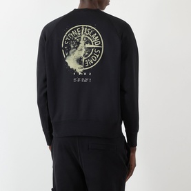 Model wearing Stone Island black sweatshirt, back view showing circular graphic logo print, styled with matching black joggers.