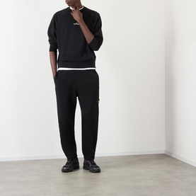 Model wearing Stone Island black polyester sweatshirt with matching black joggers and black chunky trainers.