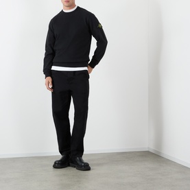 Model wearing Stone Island black cotton sweatshirt with arm badge, styled with white tee, black trousers and chunky leather shoes.