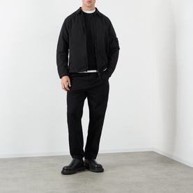 Model wearing Stone Island black cotton sweatshirt, styled with matching black zip jacket, trousers, and chunky black leather shoes.
