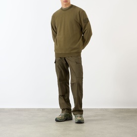 Model wearing Stone Island Compass Logo Badge Sweatshirt in green with crew neck, styled with khaki cargo trousers and trail shoes.