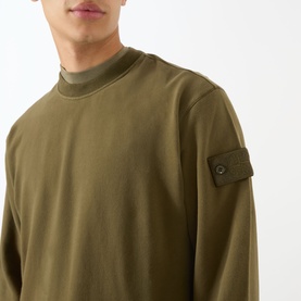 Model wearing Stone Island Compass Logo Badge Sweatshirt in green, showing sleeve badge detail and crew neckline close-up.