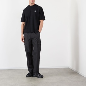 Model wearing Stone Island Compass Logo T-Shirt in black with dark cargo trousers and black chunky trainers.