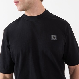Model wearing Stone Island Compass Logo T-Shirt in black, crew neck, short sleeves, with tonal square logo badge at chest.