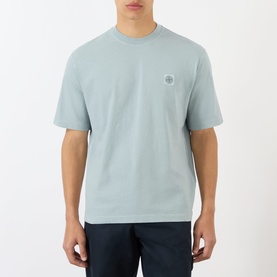 Model wearing Stone Island Compass Logo T-Shirt in ash grey, crew neck, short sleeves, with small logo patch on chest.