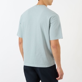 Model wearing Stone Island Compass Logo T-Shirt in ash grey, rear view, crew neck, short sleeves, styled with dark navy trousers.