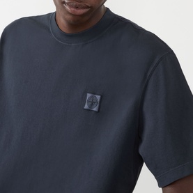 Model wearing Stone Island Compass Patch Logo T-Shirt in navy, with tonal chest logo patch detail visible at close range.