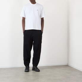 Model wearing Stone Island white cotton T-shirt with chest badge logo, styled with black trousers and black chunky trainers.
