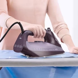Braun TexStyle 7 Pro Steam Iron in purple, shown in use gliding over a blue ironing board cover