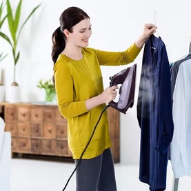 Braun TexStyle 7 Pro Steam Iron in purple, shown in use steaming a blue shirt hanging on a rail