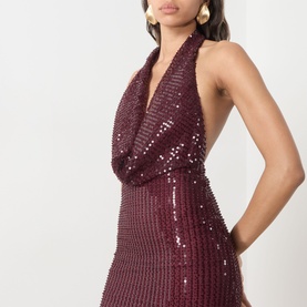 Model wearing Bardot deep plum sequin halterneck mini dress with cowl neckline, styled with gold hoop earrings