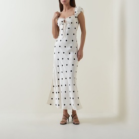 Model wearing Bardot Black Spot Dress; white midi dress with black polka dots, ruffle shoulders and flared hem, styled with brown heeled sandals
