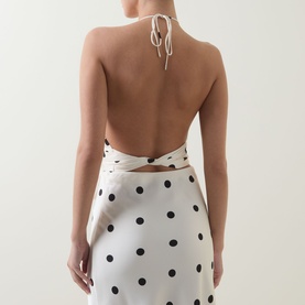 Model wearing Bardot Taryn Lace Detail Dress in canary yellow, backless halterneck with black polka dot print, low open back with tie detail.