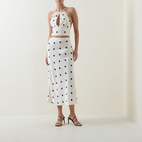 Model wearing Bardot Pheobe Polka Dot Slip Skirt in black spot, styled with matching halterneck crop top and black strappy heels.