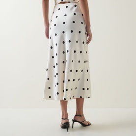 Model wearing Bardot Pheobe Polka Dot Slip Skirt in Black Spot, bias-cut satin midi length, shown from behind with black heeled sandals.