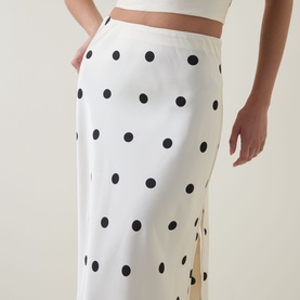 Model wearing Bardot Pheobe Polka Dot Slip Skirt in Black Spot, white midi skirt with black polka dots, bias-cut satin finish and side slit.