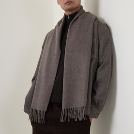 Model wearing a grey fringed scarf styled with a zip-up jacket and black turtleneck