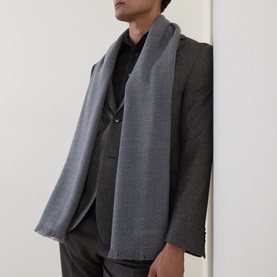 Model with grey textured scarf with frayed edges, styled over a grey suit jacket and dark trousers