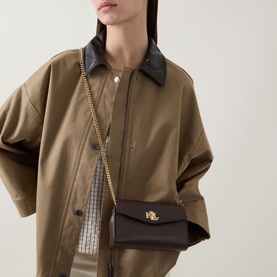 Model carrying Lauren CRS Logo Wallet Crossbody Bag in chestnut brown nappa leather, gold-toned hardware and curb chain strap
