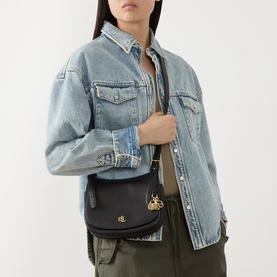 Model carrying Lauren Marcy Logo Crossbody Bag in black leather with gold-toned hardware on adjustable strap, styled with denim jacket