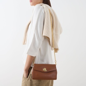 Model carrying Lauren Tanner Logo Crossbody Bag in Lauren Tan leather with gold-tone hardware and chain strap, styled with cream top and khaki