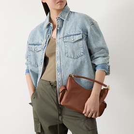 Model carrying Lauren Blaike Logo Small Shoulder Bag in Lauren Tan leather with gold-toned hardware, styled with denim shirt and khaki trousers
