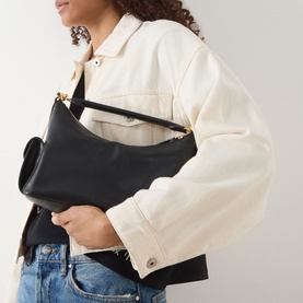 Model carrying Lauren Blaike Logo Small Shoulder Bag in black leather with gold-toned hardware, styled with cream denim jacket and blue jeans
