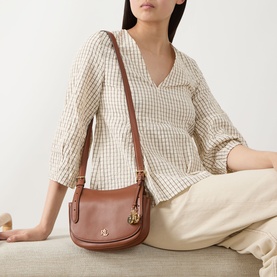 Model carrying Lauren Marcy Logo Crossbody Bag in Lauren Tan leather with gold-toned hardware and adjustable strap, styled with check blouse