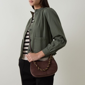 Model carrying Lauren Marcy Charm Shoulder Bag in chestnut brown leather with gold-tone chain strap, styled with olive jacket and striped top.