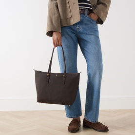 Model carrying Lauren Keaton 26 Tote Bag in chestnut brown with gold-tone hardware and carry handles, styled with jeans and blazer