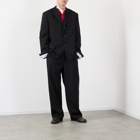 Model wearing Loewe black wool casual jacket with matching trousers, red waistcoat, white shirt, and black leather shoes.