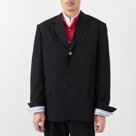 Model wearing Loewe black wool casual jacket with three-button front, notch lapels, styled with red shirt and striped cuffs visible at hem.