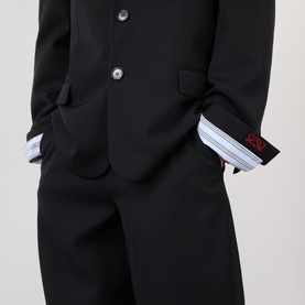 Model wearing Loewe black wool casual jacket with silver buttons, styled with striped shirt cuffs and matching wide-leg trousers visible.