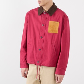 Model wearing Loewe red cotton casual jacket with brown corduroy collar, tan chest pocket, and button-front fastening, styled with cream trousers