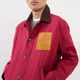Model wearing Loewe red cotton casual jacket with brown corduroy collar, mustard suede chest pocket, and grey layered knitwear beneath.