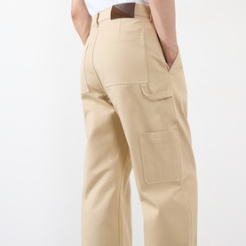 Model wearing Loewe beige cotton casual trousers, rear view showing large patch pocket and wide-leg fit, styled with white top and brown belt.