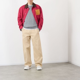 Model wearing Loewe beige casual cotton trousers, styled with a red jacket, grey sweatshirt and white trainers.