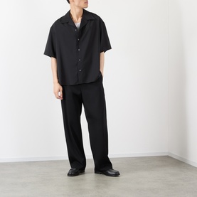 Model wearing Loewe Solid Camp Shirt in black wool with camp collar and short sleeves, styled with black wide-leg trousers and loafers.