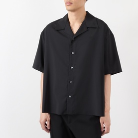Model wearing Loewe Solid Camp Shirt in black, with camp collar, short sleeves, and front button fastening, styled with black trousers.