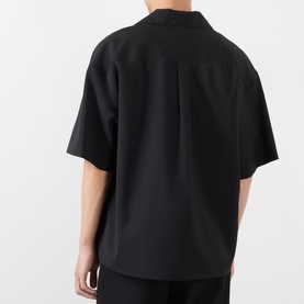 Model wearing Loewe Solid Camp Shirt in black, showing rear box pleat detail, dropped shoulders and short sleeves, styled with black trousers.