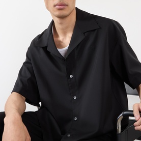 Model wearing Loewe Solid Camp Shirt in black, short-sleeve wool camp collar shirt with front button fastening, styled with a white T-shirt.