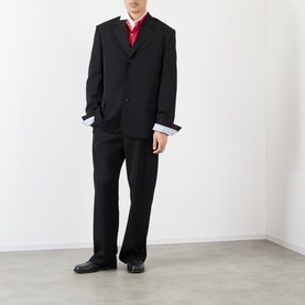 Model wearing Loewe black wool casual trousers styled with a matching black blazer, red polo shirt and black leather shoes.