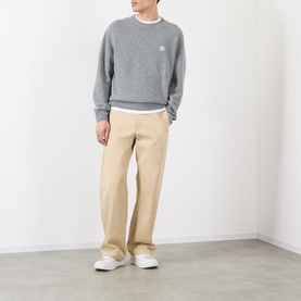 Model wearing Loewe Anagram Logo Sweater in grey melange wool crew neck, styled with beige trousers and white trainers.