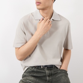 Model wearing Loewe grey cotton polo shirt with open collar, styled with dark jeans and black belt.