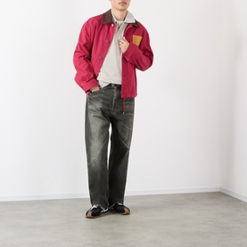 Model wearing Loewe grey cotton polo, styled with red zip-up jacket, dark wash jeans and black loafers