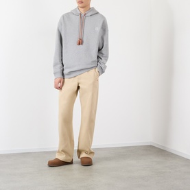 Model wearing Loewe grey melange cotton hoodie with brown drawstring detail, styled with beige wide-leg trousers and brown slippers.