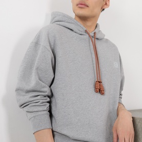 Model wearing Loewe grey melange cotton hoodie with brown leather drawstring detail and small chest logo embroidery.